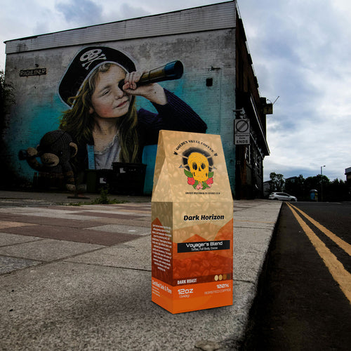 Coffee bag labeled 'Dark Horizon' on a sidewalk with a mural of a child holding a spyglass in the background.