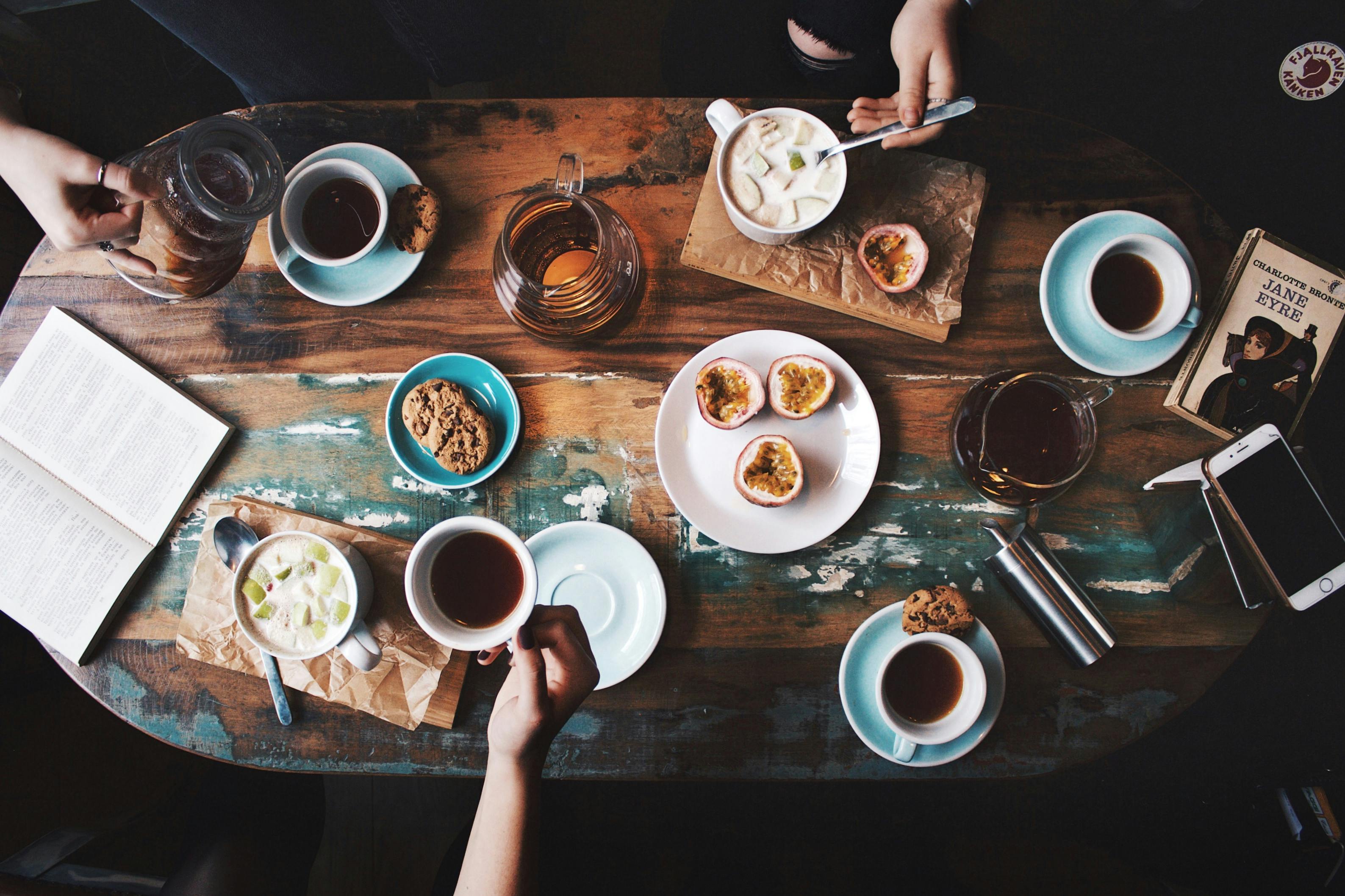 Top-down view of a wooden table with coffee cups, pastries, and snacks.